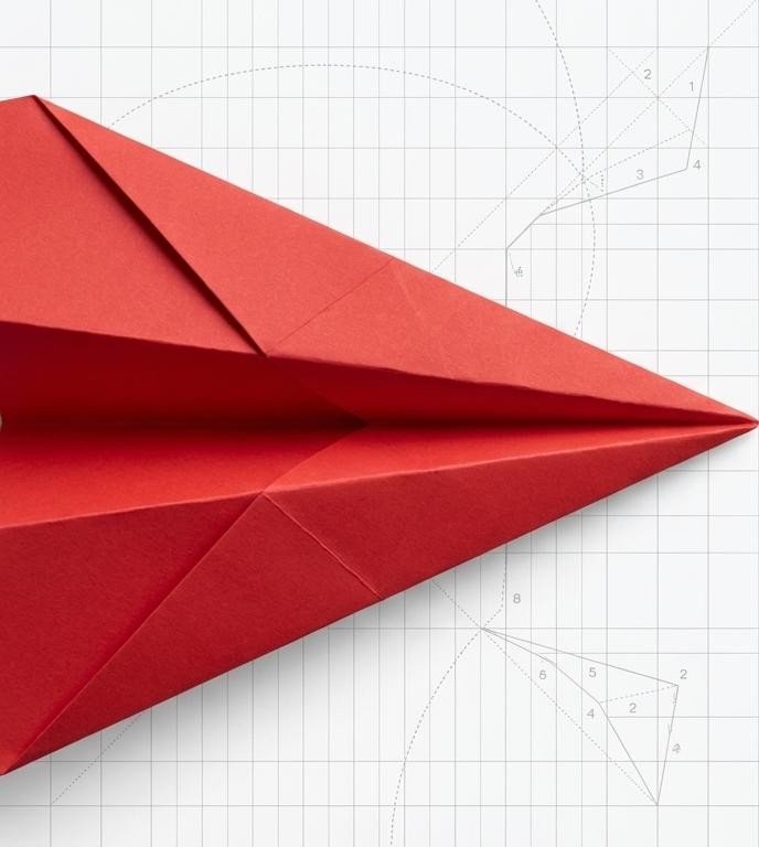 A folded red paper plane on a drafting grid